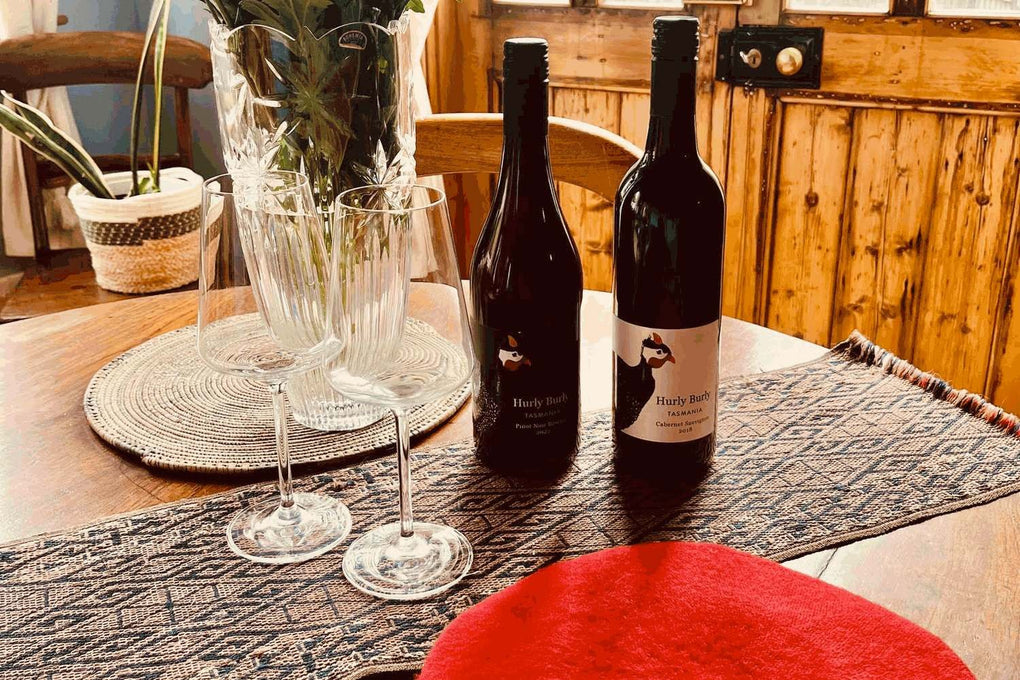 Hurly Burly Pinot Noir Reserve and Cabernet Sauvignon on a rustic table with a red French beret